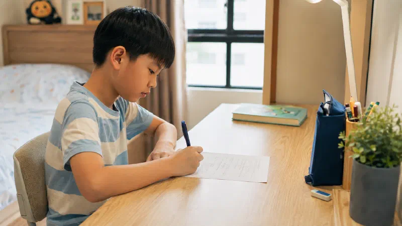 Boy writing with a closed textbook beside him.